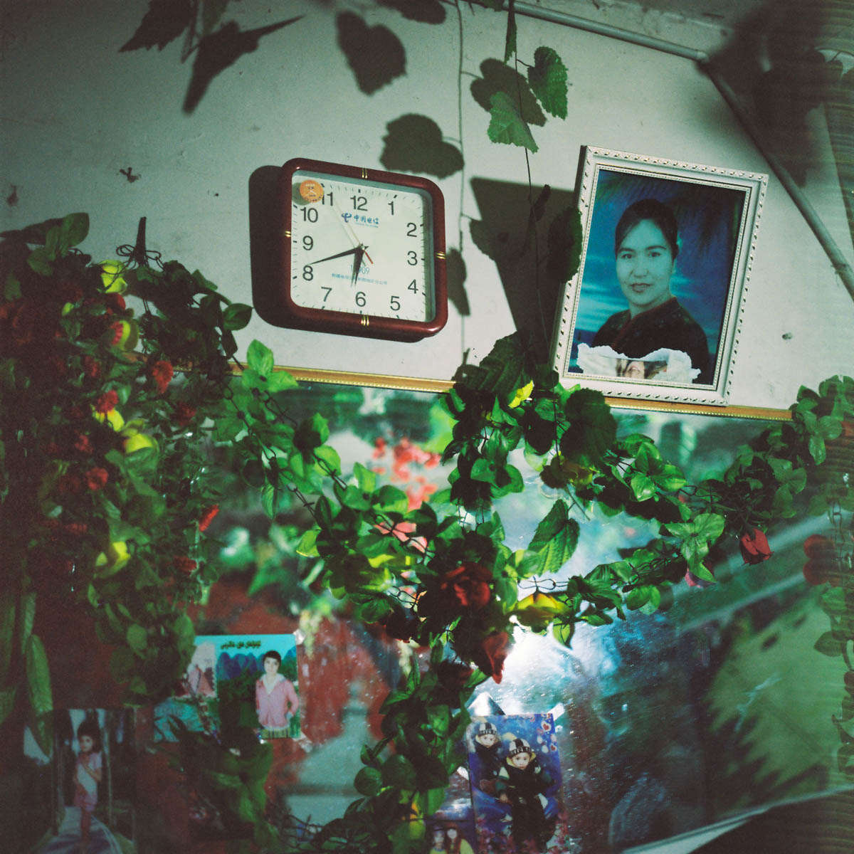 Interior of a photographer's shop - Interior of a photo shop the picture of his mother is hanging on the wall next to a clock and some plastic vine.  Hotan, Xinjiang, China 2012. 