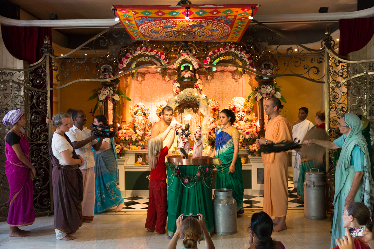 Im Zürcher Tempel der Hare Krishna-Bewegung werden gerade die Murtis, die Statuen von Krishna und seiner Gefährtin Radha, während eines Rituals übergossen. Daneben steht in der gelben Mönchstracht der Vorsteher des Tempels, Krishna Premarupa. ISKCON Tempel, Zürich, August 2017