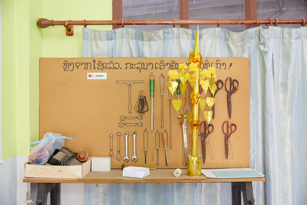 Each tool at its designed place. Japan’s Official Development Assistance sponsored sewing machines and tools at the Vientiane Capital Skill Development Center. The golden tree is a typical offering for the Buddha in Laos. It symbolizes the Bodhi Tree under which Siddhartha Gautama is said to have attained enlightenment. Vientiane, Laos, November 2018.